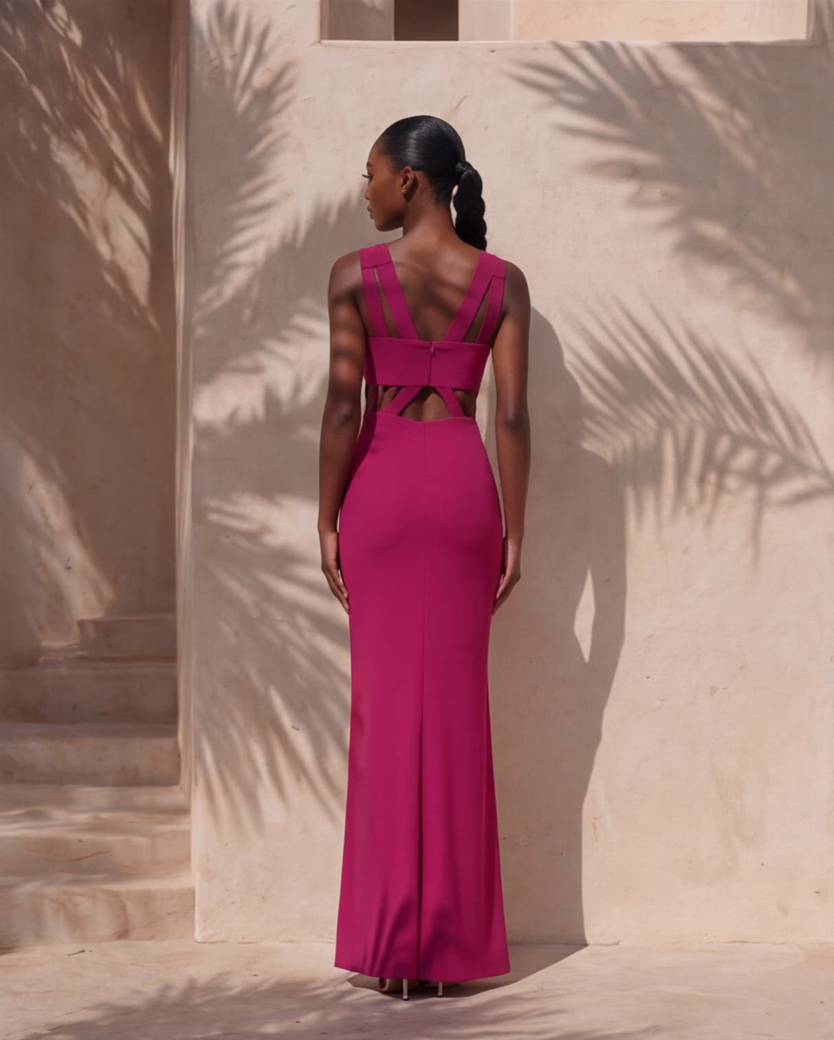 Back view — the crossed straps and open back of the dress, a braided ponytail falling between the shoulders.