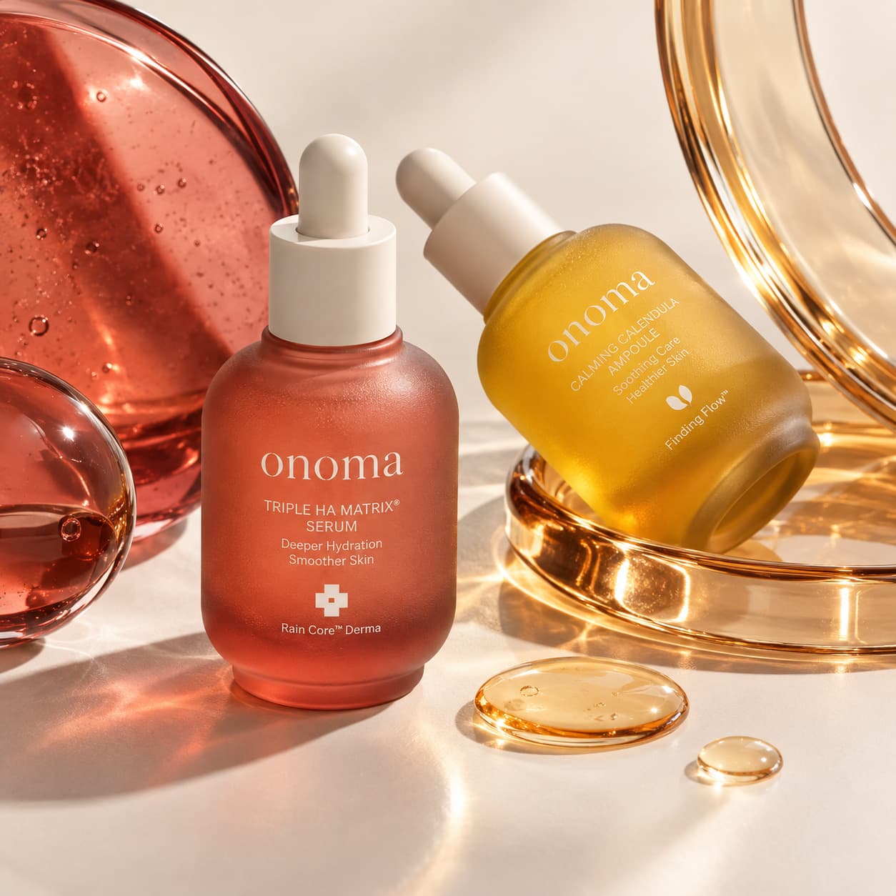 Macro still life — the red triple HA matrix serum and the amber calming calendula ampoule among tinted glass discs and oil droplets.