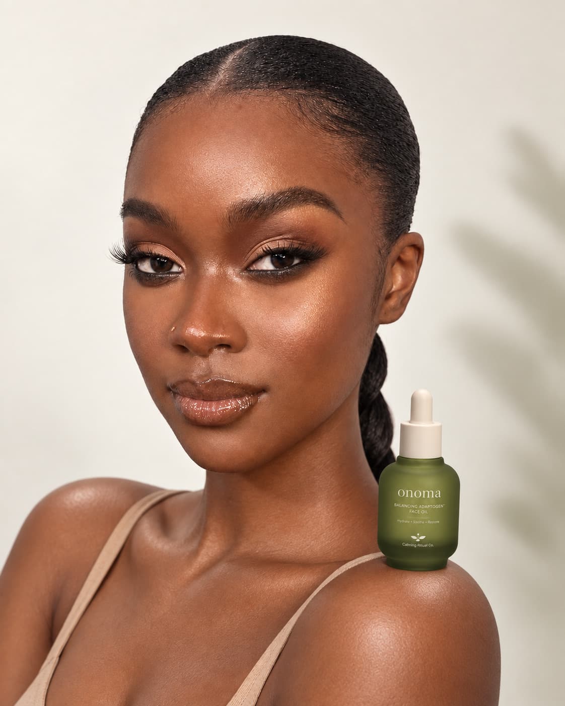Beauty portrait — a model with a sleek braid and warm bronze makeup beside the green balancing adaptogen face oil.